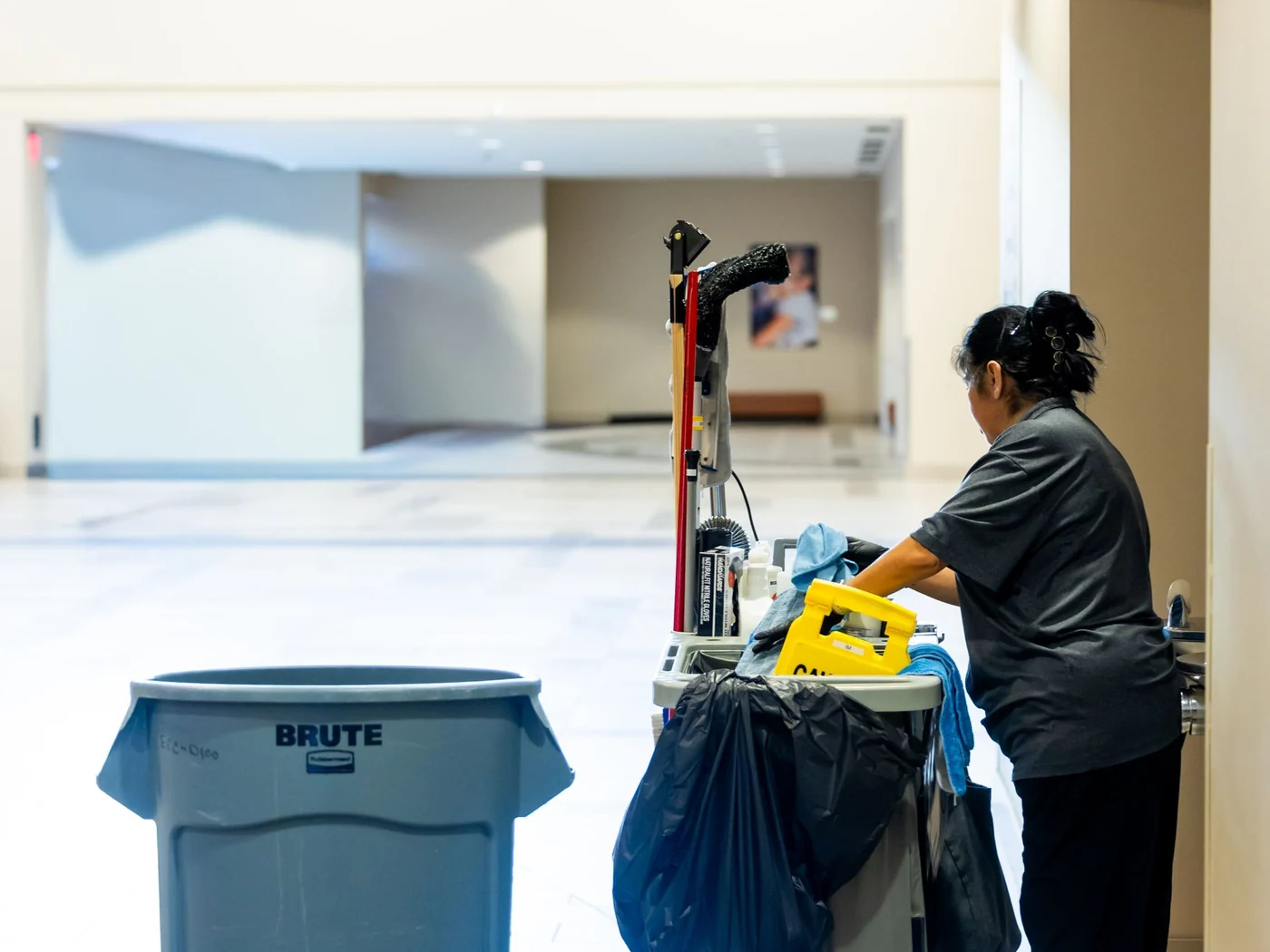 Cleaner servicing a commercial building corridor with a janitorial cart